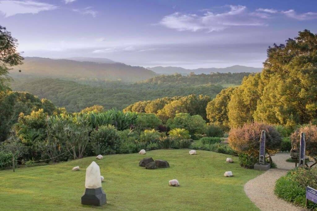 A serene view of the lush Byron Bay hinterland with rolling hills and forest, featuring a grassy area with crystals and stones, representing the natural beauty encountered on Byron Bay day tours. Ideal for those looking for 'Byron day deals' to explore this stunning region.