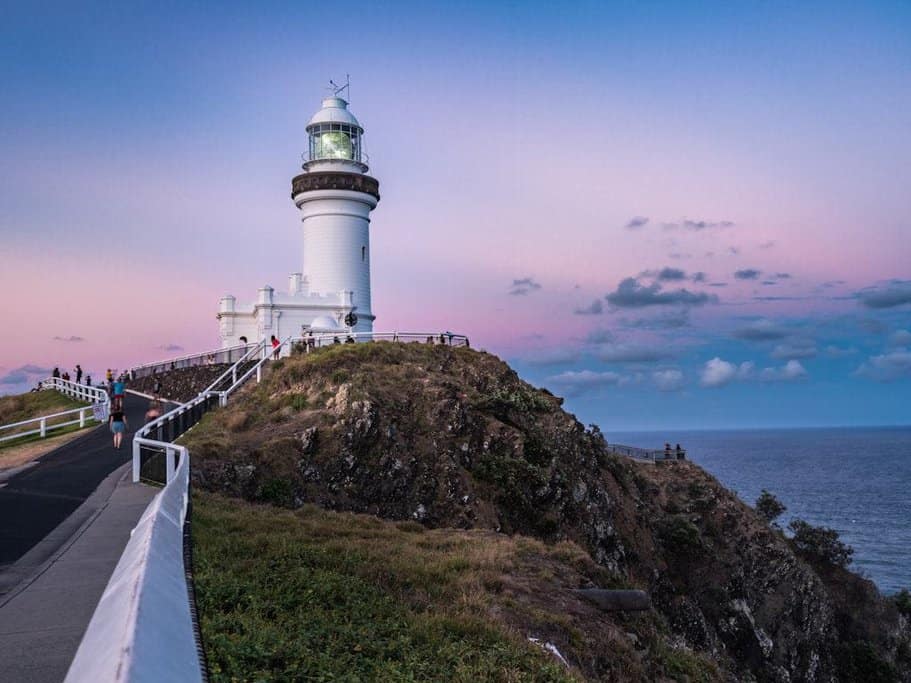 The Cape Byron Lighthouse stands majestically on a cliff under a pastel sky at sunset, a highlight of Byron Bay day tours. Ideal for visitors seeking 'Byron day deals' that include iconic landmarks and scenic views.