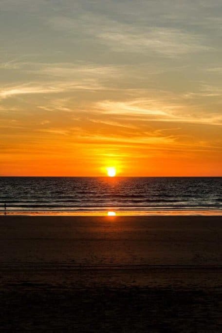 Sunset over Cable Beach, one of the popular beaches in Western Australia, showing the sun dipping into the horizon with golden hues reflecting on the wet sand and a solitary figure admiring the view