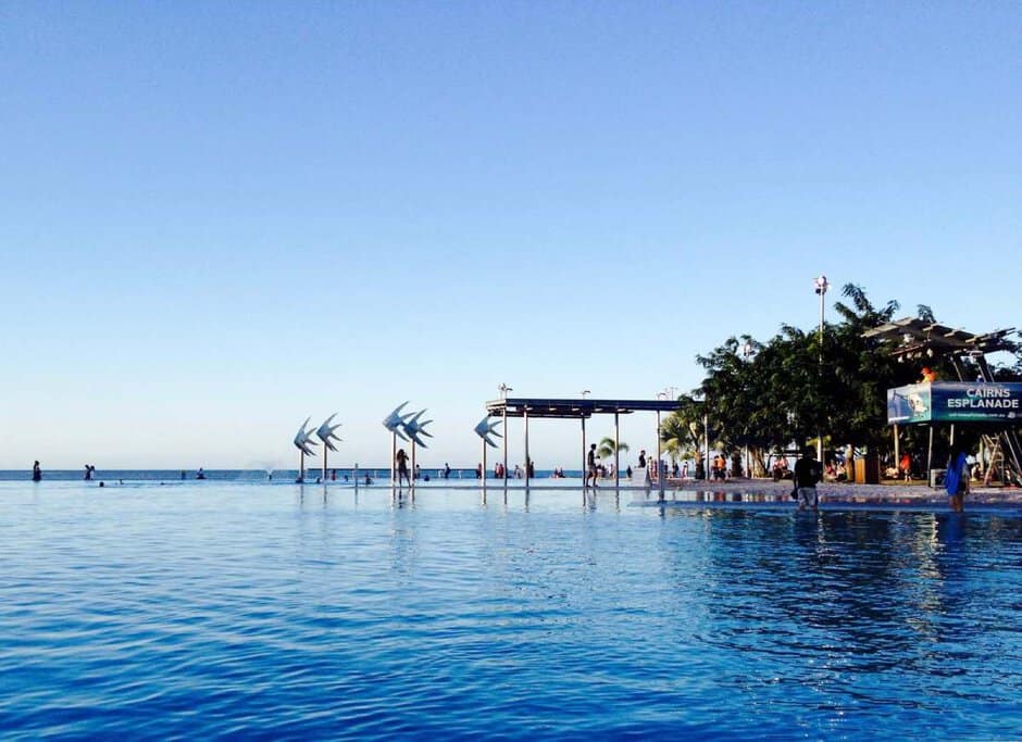 The Cairns Esplanade Lagoon, a popular waterfront attraction with clear blue water, public swimming areas, and artistic fish sculptures. This image represents the outdoor lifestyle and tropical appeal, a key factor when considering the pros and cons of living in Cairns.