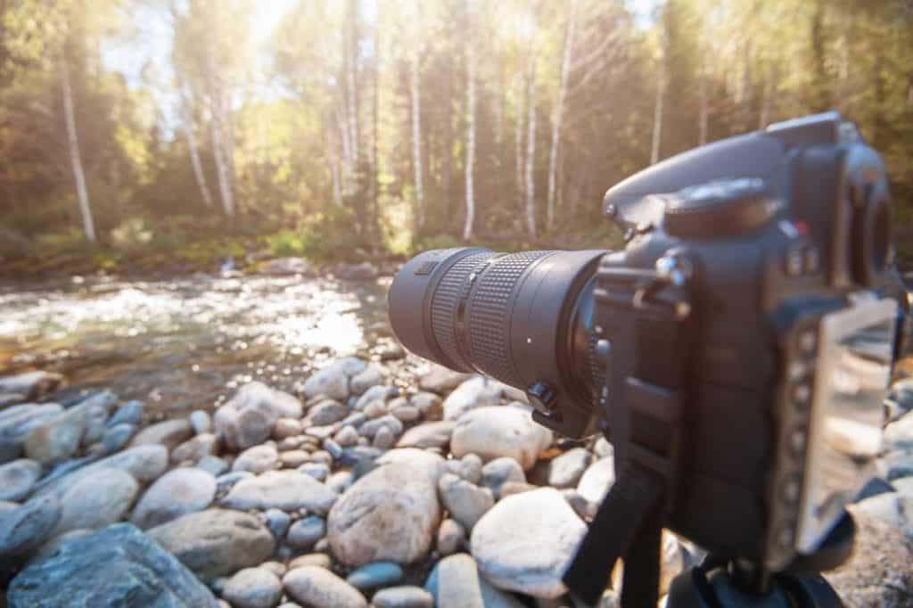 A professional camera with a telephoto lens set up on a tripod, capturing a scenic riverside view with sunlit trees in the background. This setup is ideal for photographers exploring The Most Scenic Photography Spots on the Great Ocean Road, where nature and landscape photography opportunities are endless.