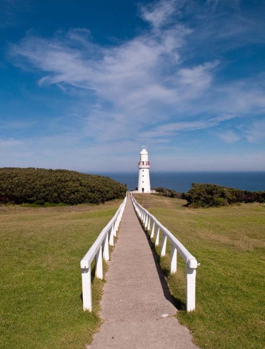 A scenic pathway leading to the iconic Cape Otway Lighthouse, surrounded by lush greenery and blue skies, a highlight along popular hiking trails in Victoria, Australia.