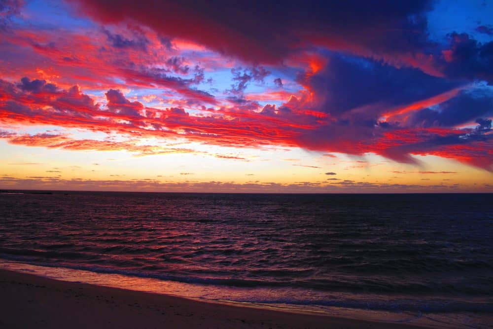 Vibrant sunset over the ocean at Cape Range National Park, Western Australia, with rich hues of red and purple reflecting off the water. This image showcases one of the most stunning sunset locations in Australia, aligning with the blog post on must-see sunsets.