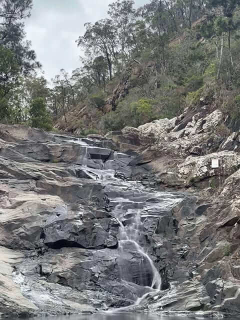 A serene cascade at Cedar Creek falls, surrounded by rugged rocks and lush greenery, offering a tranquil escape on a 9-day Gold Coast itinerary.