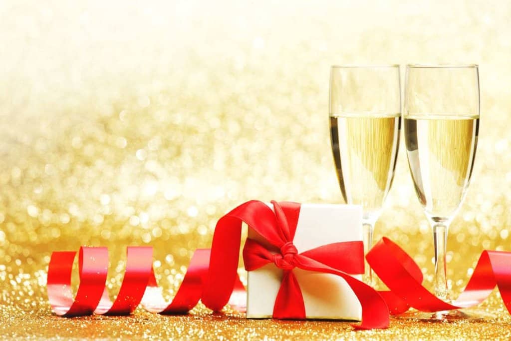 \Two champagne glasses beside a gift box wrapped with a red ribbon, representing elegant and festive Kris Kringle gifts for Christmas celebrations.
