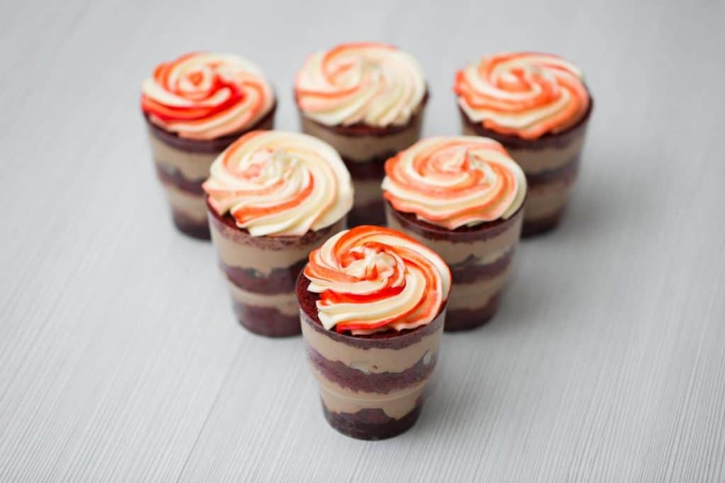 Red velvet and mousse trifle desserts in plastic cups, topped with swirled cream, showcasing a festive treat perfect for celebrating Christmas desserts in Australia.