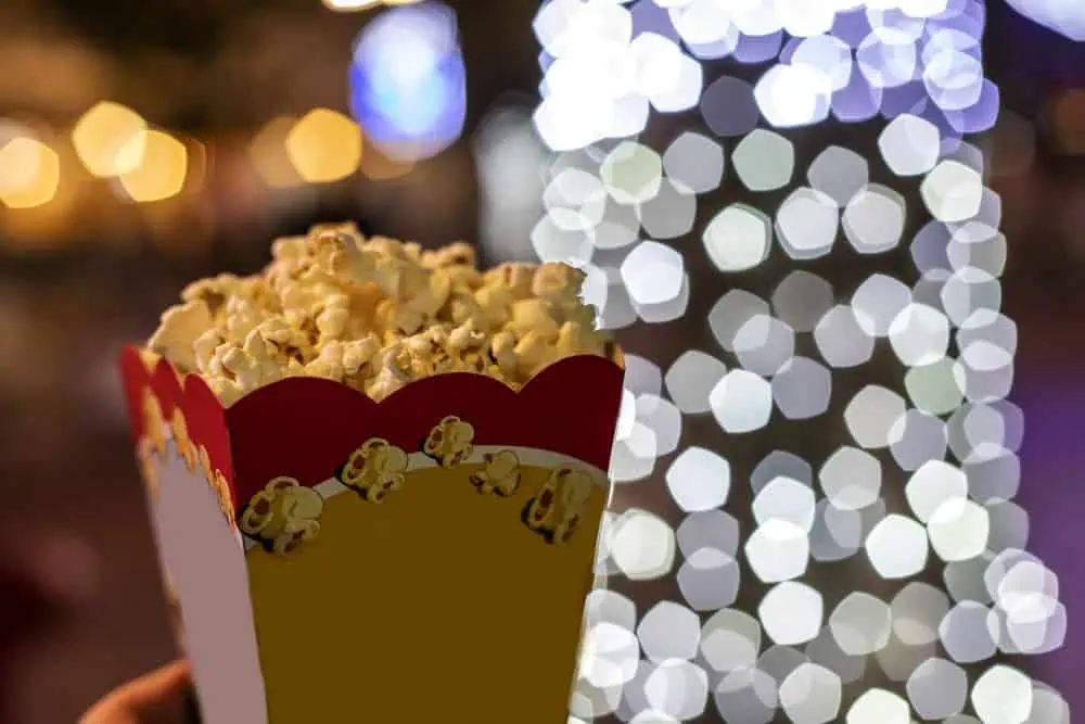 A box of popcorn held up against a backdrop of festive Christmas lights. Enjoying Christmas movie screenings is one of the popular Melbourne Christmas experiences, bringing holiday cheer to the city's vibrant festive season.