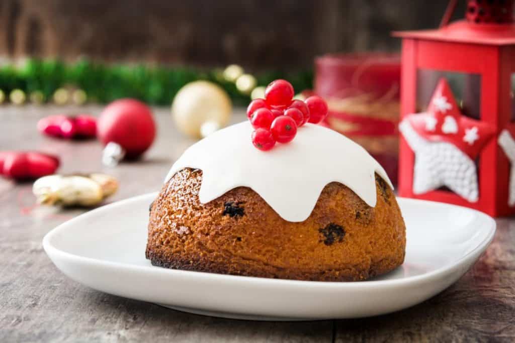 Traditional Christmas pudding topped with white icing and red berries, a classic dessert often enjoyed during Australia's Christmas desserts celebrations.