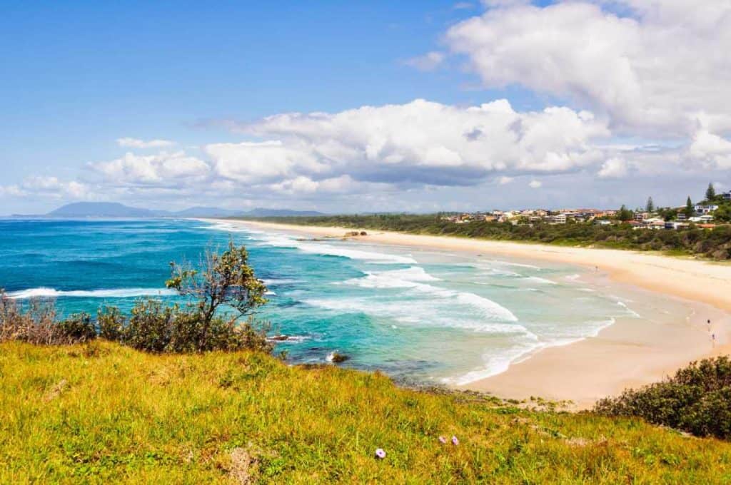 Vibrant coastal view of Port Macquarie’s beach with waves rolling in under a partly cloudy sky, a picturesque highlight along the scenic Sydney to Byron Bay drive.