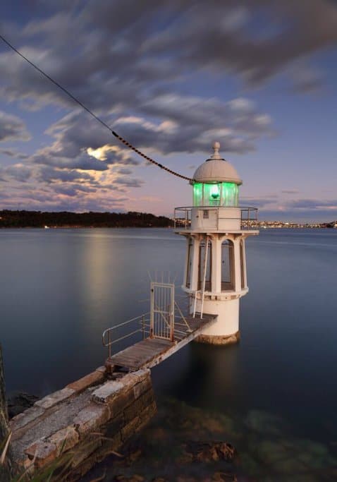 Cremorne Point Lighthouse at sunset, with a calm Sydney Harbour and the city lights twinkling in the background. This image highlights one of Sydney’s hidden gems for watching sunset locations in Australia, tying into the blog post about must-see sunsets.