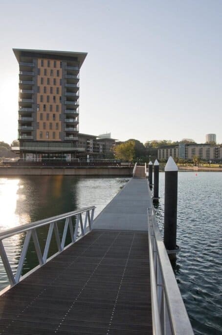 View of a modern apartment building and waterfront boardwalk in Darwin, Northern Territory, at sunset. This image reflects the relaxed lifestyle and scenic living options often mentioned in the pros and cons of living in Darwin.