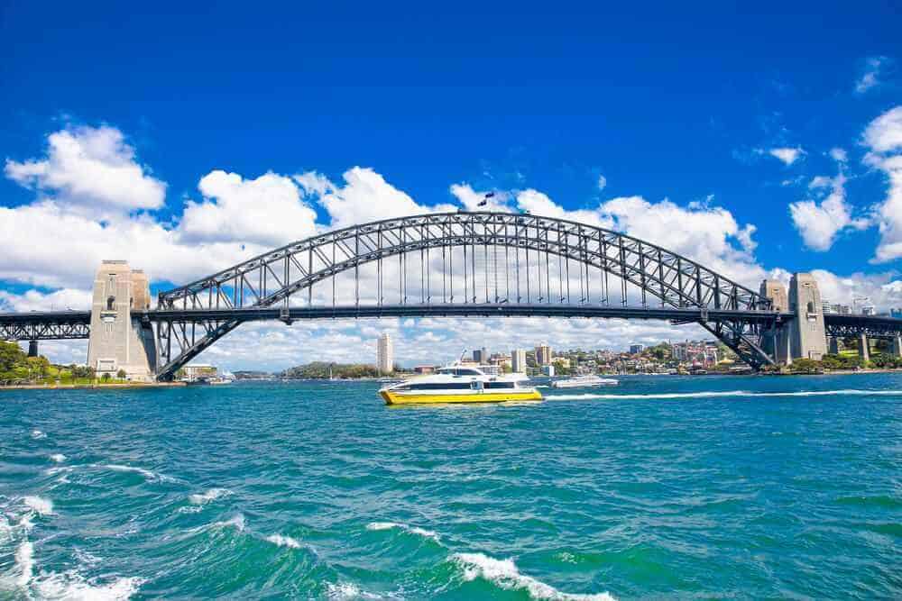 The Sydney Harbour Bridge under a bright blue sky with a ferry passing below, a popular sight on food tours in Sydney, Australia, especially during a delightful lunch cruise.