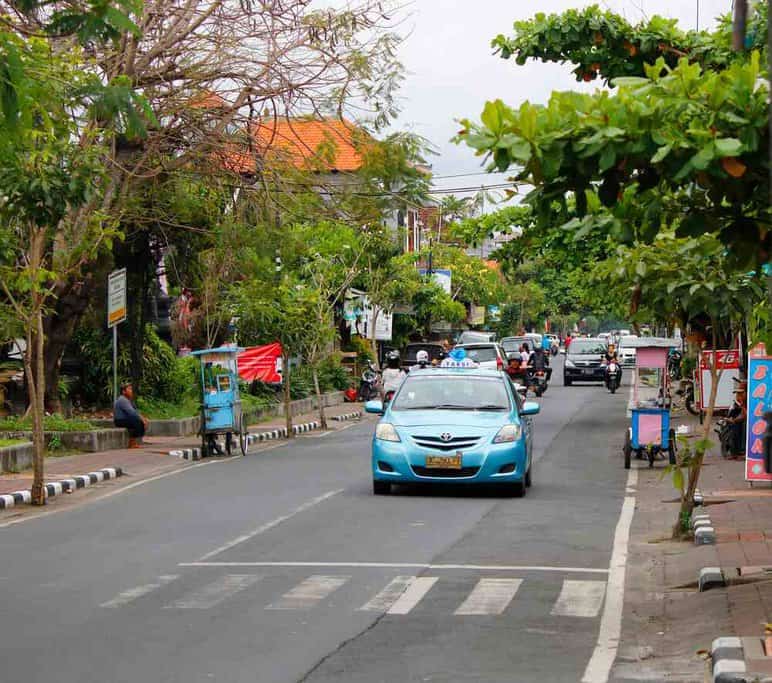 A Blue Bird taxi cruising on a lively street in Bali, serving as a popular alternative for visitors who might otherwise look for an Uber in Bali.