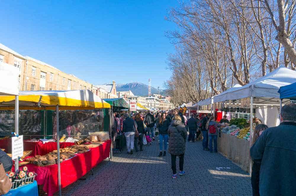 Salamanca Market in winter, a hub of activity in Hobart where visitors browse local crafts and produce with Mount Wellington in the distance, perfect for those interested in winter activities in Hobart.