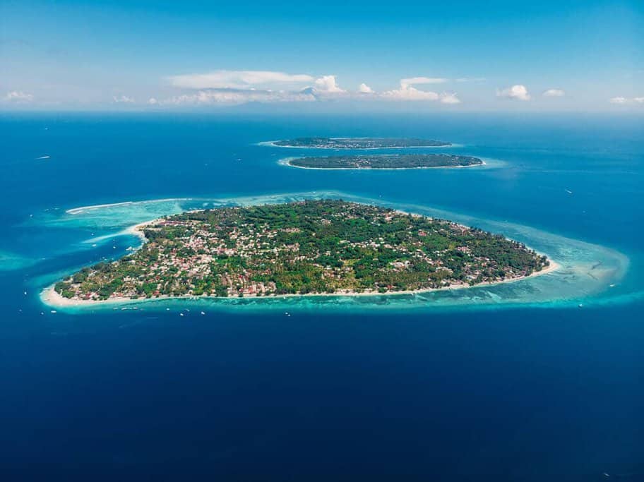 Aerial view of the Gili Islands, highlighting the clear turquoise waters surrounding the lush, densely populated islands, a prime destination for travelers looking for serene beauty and things to do in the Gili Islands.