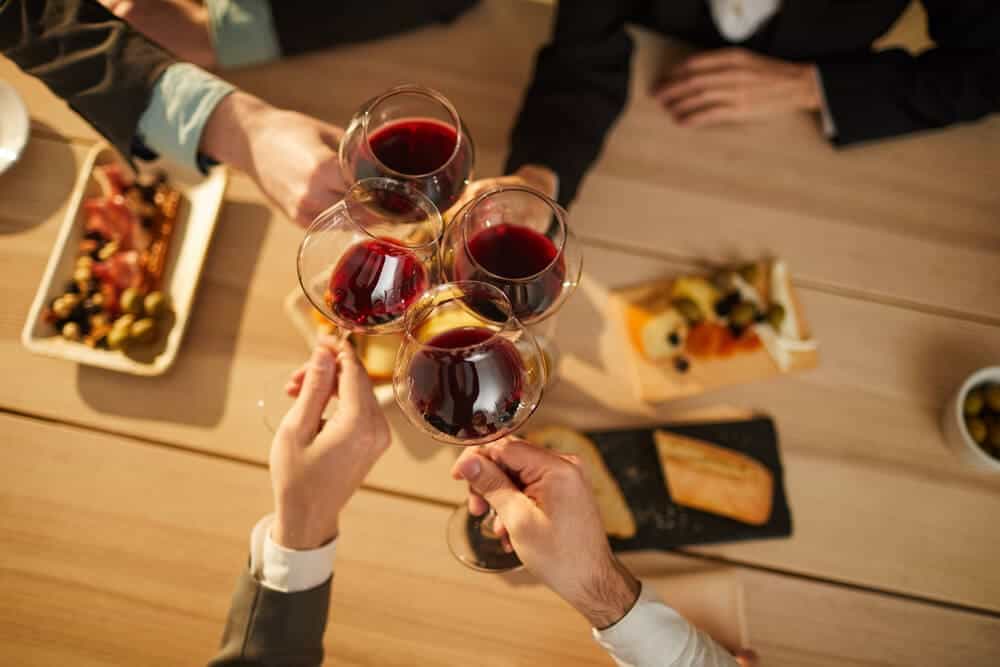A group of hands toasting with glasses of red wine over a table adorned with gourmet snacks, capturing the social and enjoyable atmosphere of Hobart wine tours.