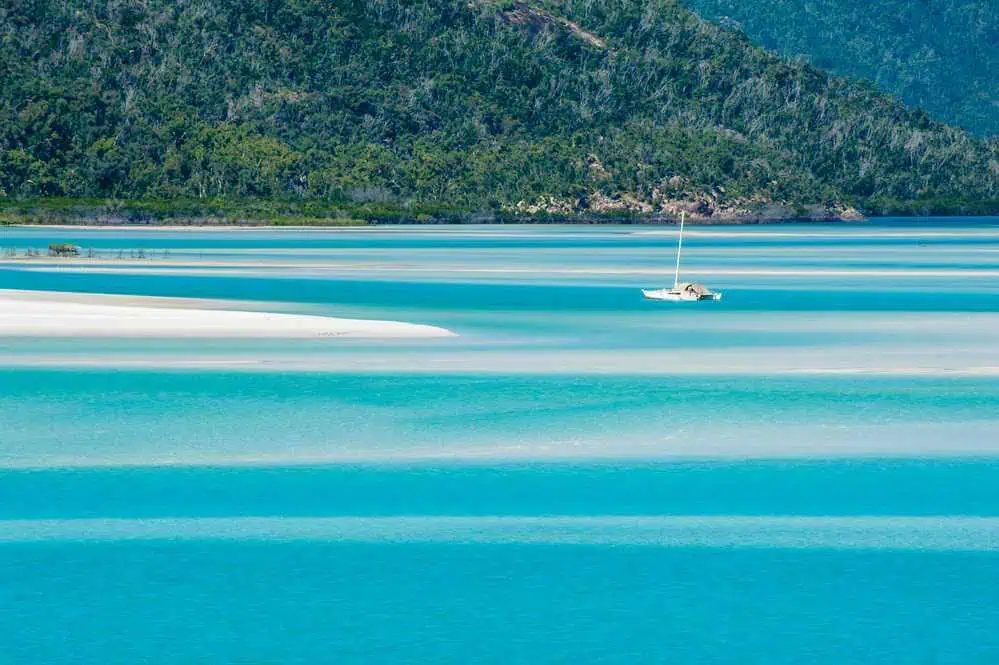 Sailboat navigating the calm turquoise waters near the pristine silica sands of Whitehaven Beach, a jewel in the Whitsundays, often featured in comparisons with the tropical allure of Cairns.