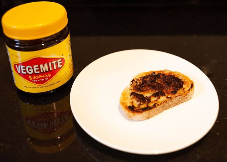 A slice of toast with Vegemite beside its jar, a staple spread in Australian homes and a taste often experienced on food walking tours in Sydney.
