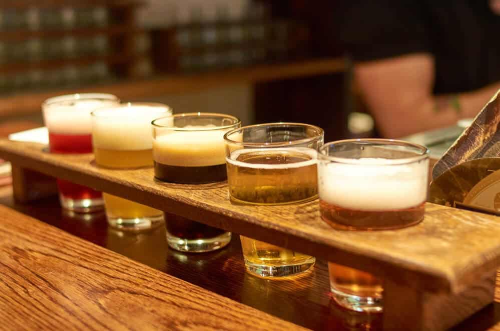 An inviting wooden beer flight board lined with a variety of beers, from a frothy stout to a clear golden ale, ready for tasting on a Brisbane brewery tour, capturing the essence of local craft beer culture.