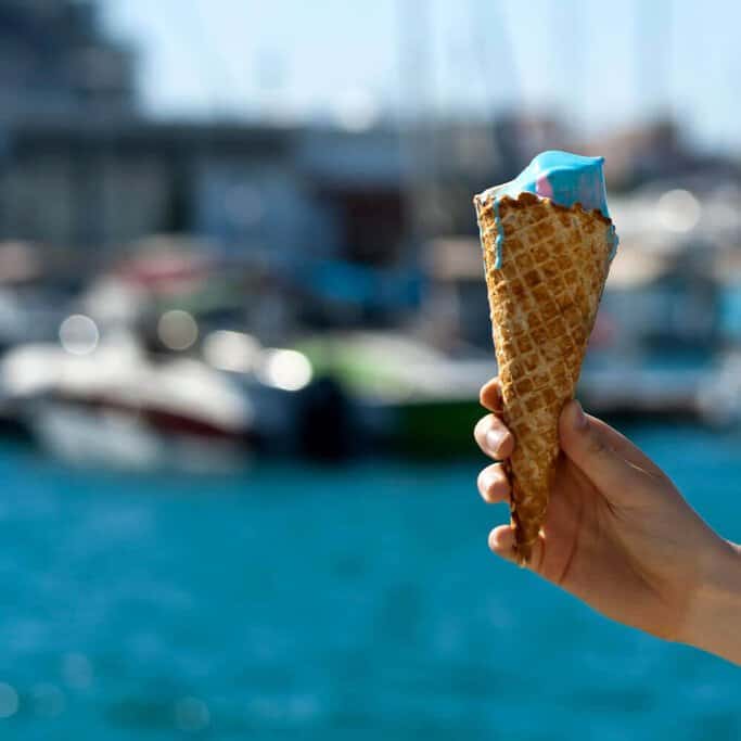 A hand holding a vibrant blue ice cream cone with the backdrop of Sydney's harbour, a refreshing treat often savoured on Sydney's best food tours.