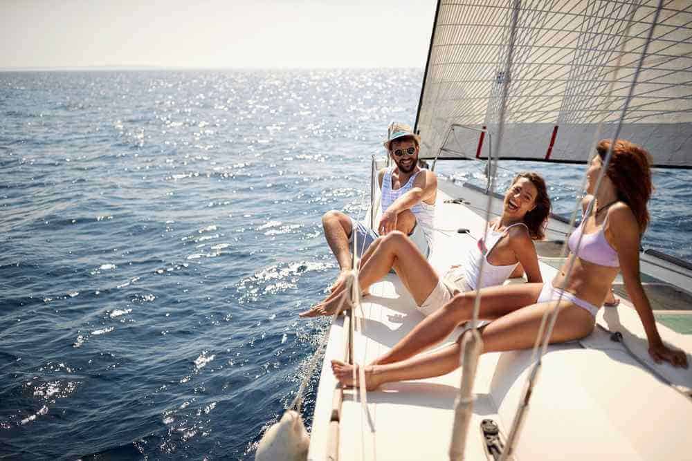 Friends laughing and relaxing on the deck of a yacht under the bright sun, enjoying a private Sydney boat tour on the glittering waters.