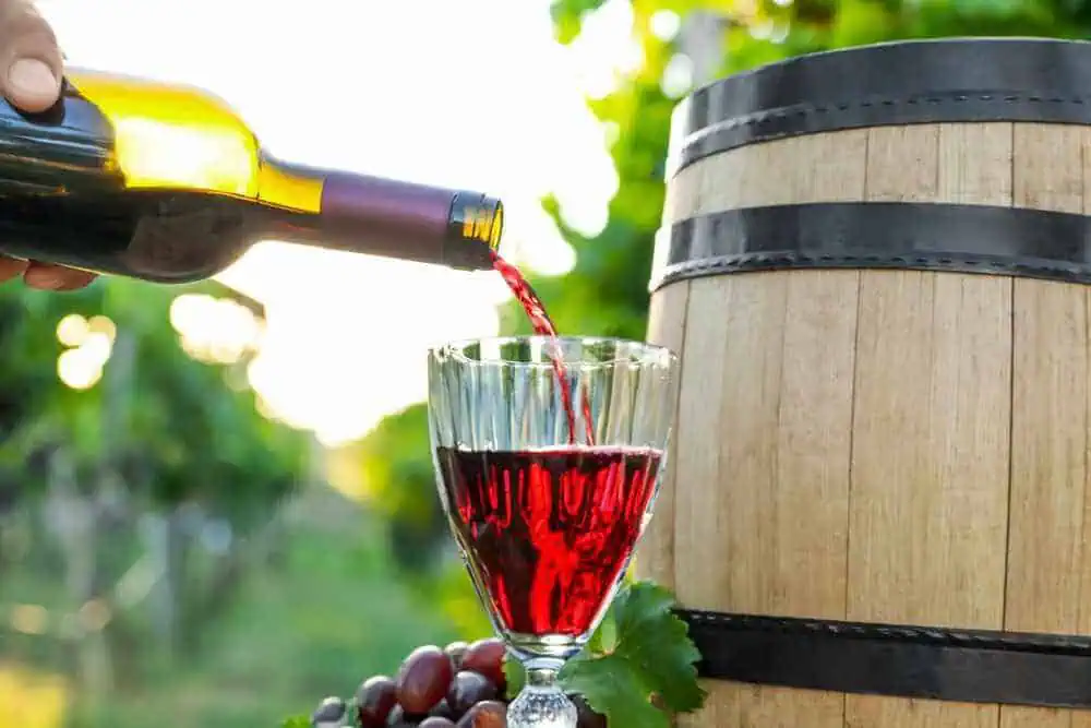 Red wine being poured into a glass beside an oak barrel, with grapes in the background, depicting the enjoyable activities of a Hunter Valley day trip from Sydney.