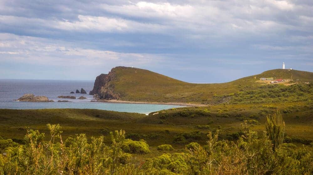 A scenic view of Cape Bruny Lighthouse on South Bruny Island, Tasmania, with lush greenery in the foreground and the ocean in the distance, a serene spot often included in travel itineraries for exploring Tasmania's natural beauty.