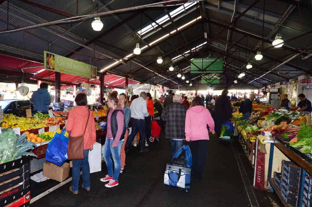 Bustling indoor market scene with stalls of fresh produce and shoppers, a cosy and vibrant thing to do in Melbourne in winter.