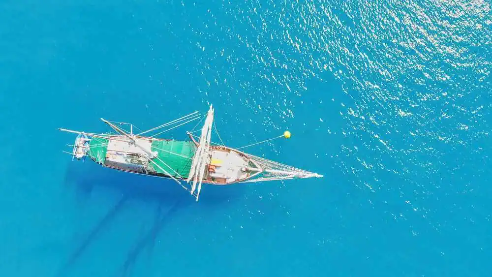 Top-down aerial view of a schooner anchored in the sparkling azure waters, capturing the essence of sailing in the idyllic Whitsundays, comparable to the adventure-filled maritime experiences near Cairns.