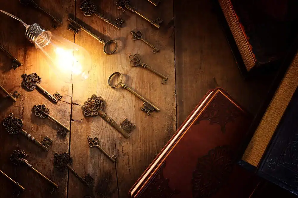An illuminated lightbulb and a collection of intricate old keys spread out on a wooden table, alongside vintage books, setting the mysterious and adventurous ambiance of an escape room experience in Melbourne, perfect for a winter activity.