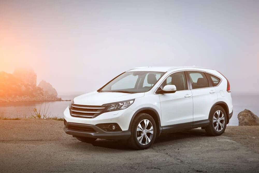 A white SUV parked on a gravel lot at sunset with a scenic view of the ocean and rocky cliffs, representing a convenient option for travellers using a private driver to enjoy picturesque sunsets.