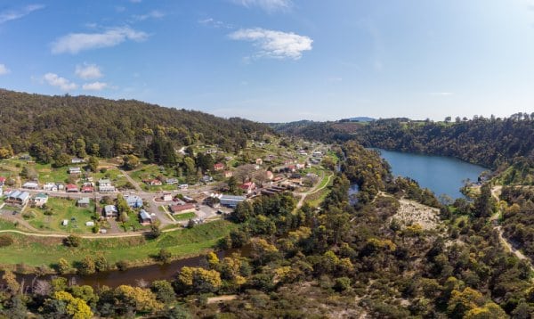 Aerial view of Derby, Tasmania, showcasing the picturesque township nestled among lush hills with a view of the tranquil lake, highlighting the destination's natural beauty and charm, a perfect setting for luxury cabin retreats.