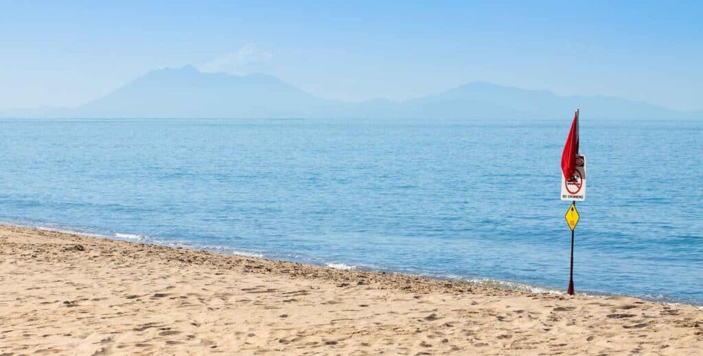 A deserted beach with a 'No Swimming' sign and a warning about jellyfish, illustrating the need to exercise normal precautions in Australia. This image highlights the importance of paying attention to local safety signs to avoid potential hazards while enjoying the beach.