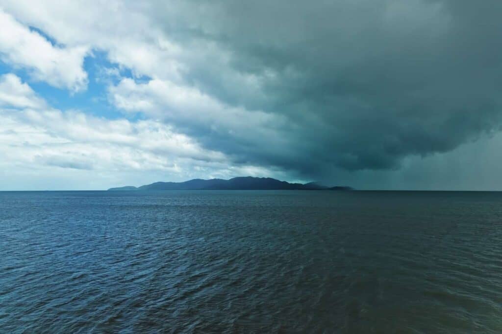 A dark and stormy sky over the ocean, with a distant island under the looming clouds, indicating the approach of a cyclone. This image relates to the topic of 'natural disasters,' highlighting the importance of being prepared for severe weather events in Australia, such as cyclones, which are common in certain regions.