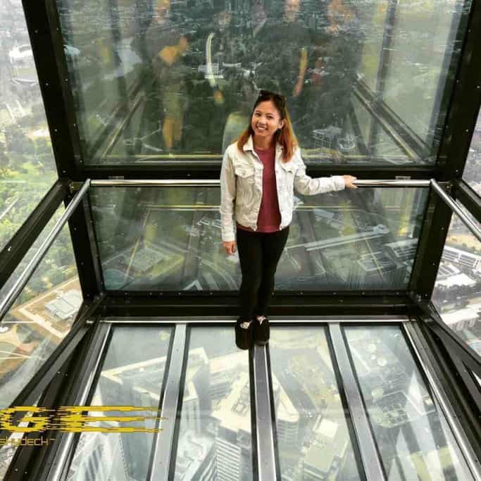 Me standing inside the Eureka Skydeck's glass cube, looking out over the Melbourne skyline. The glass floor and walls provide a thrilling view straight down to the city below, showcasing one of the most Instagrammable places in Melbourne. The image captures the excitement and breathtaking perspectives available at the Eureka Skydeck.