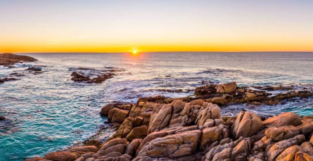Golden sunset over the rugged coastline of Friendly Beaches in Tasmania, with waves gently crashing against the rocky shore. This secluded spot is a perfect example of Tasmania's hidden coastal gems, offering pristine waters and breathtaking views away from the crowds.
