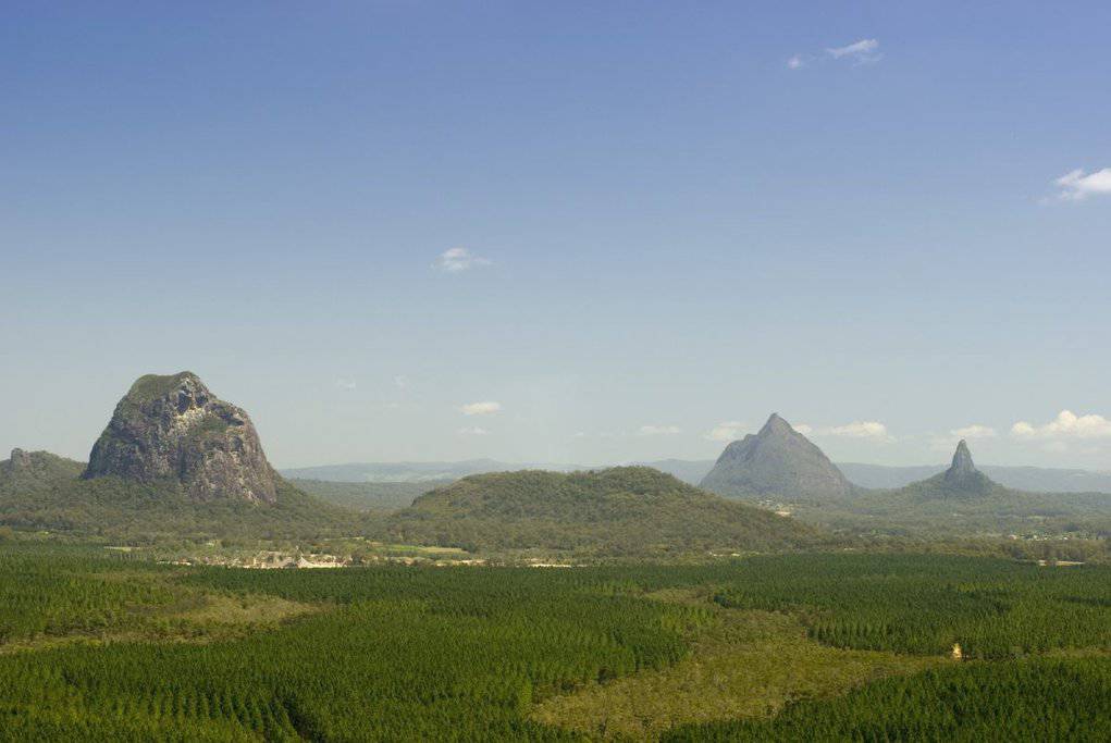 A panoramic view of the iconic Glass House Mountains rising above dense greenery on the Sunshine Coast, a highlight of scenic drives in Queensland.