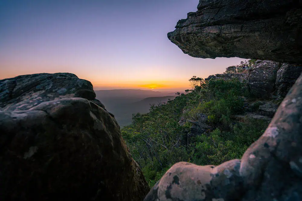Sunset view from the rugged cliffs of the Grampians National Park, with the sky glowing in soft orange and purple hues. This image showcases one of the top sunset spots in Australia, complementing the blog post about must-see sunset locations.