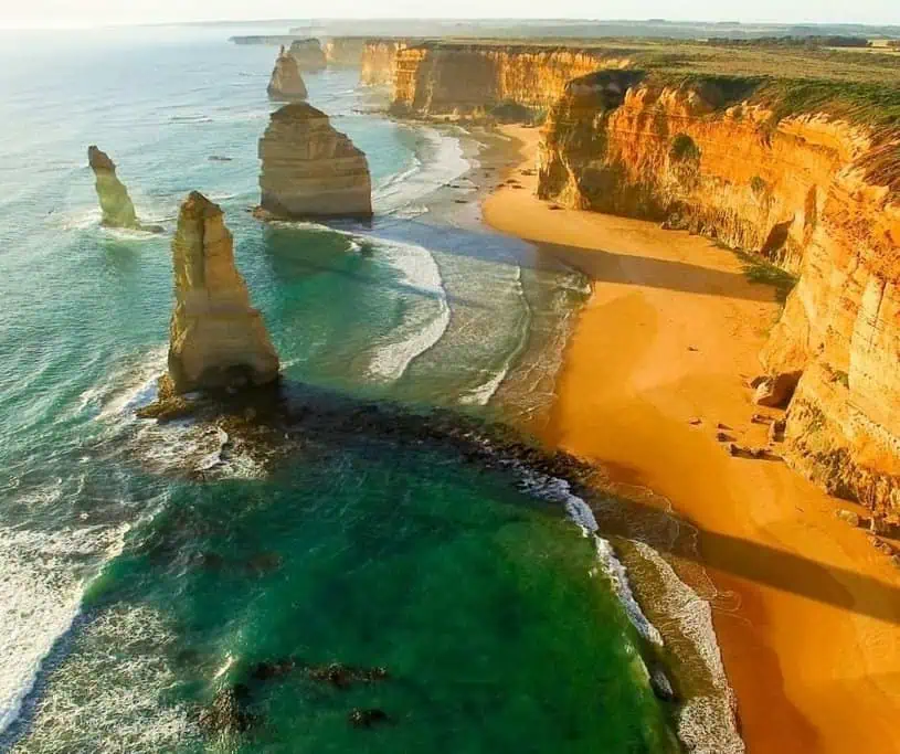 An aerial view of the Twelve Apostles along the Great Ocean Road, with dramatic limestone stacks rising from the turquoise waters, showcasing one of Australia's most iconic coastal landscapes. This image is perfect for an Australia travel guide, highlighting must-see destinations along this famous route.