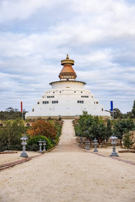 The Great Stupa of Universal Compassion in Bendigo, Victoria, a Buddhist monument with a striking white and gold tiered design, set against a cloudy sky. This spiritual landmark is part of the city's cultural diversity, which plays a role in the discussion of the benefits and drawbacks of living in Bendigo.