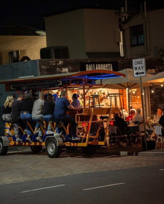 A group of people enjoying a nighttime HandleBar Adelaide tour, pedaling past Ballaboosta restaurant. This image illustrates the fun and lively experience of the HandleBar Adelaide Progressive Dinner Tour, which includes stops at renowned restaurants for a unique culinary adventure.