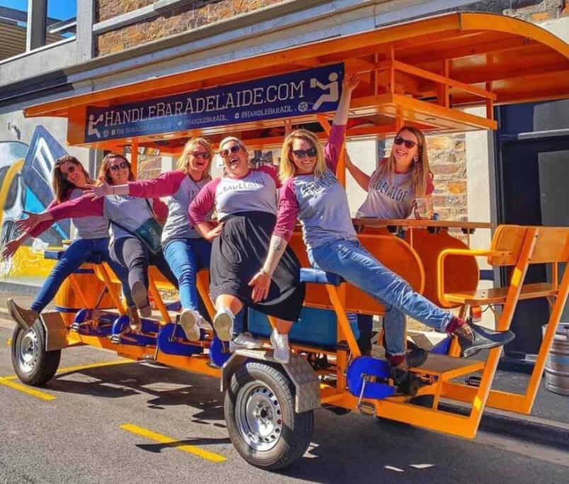A group of friends enjoying a HandleBar Adelaide tour on a sunny day, sitting on a pedal-powered vehicle. This image showcases the fun and unique experience offered by HandleBar Adelaide, highlighting the vibrant and social atmosphere of their tours through the city's streets.