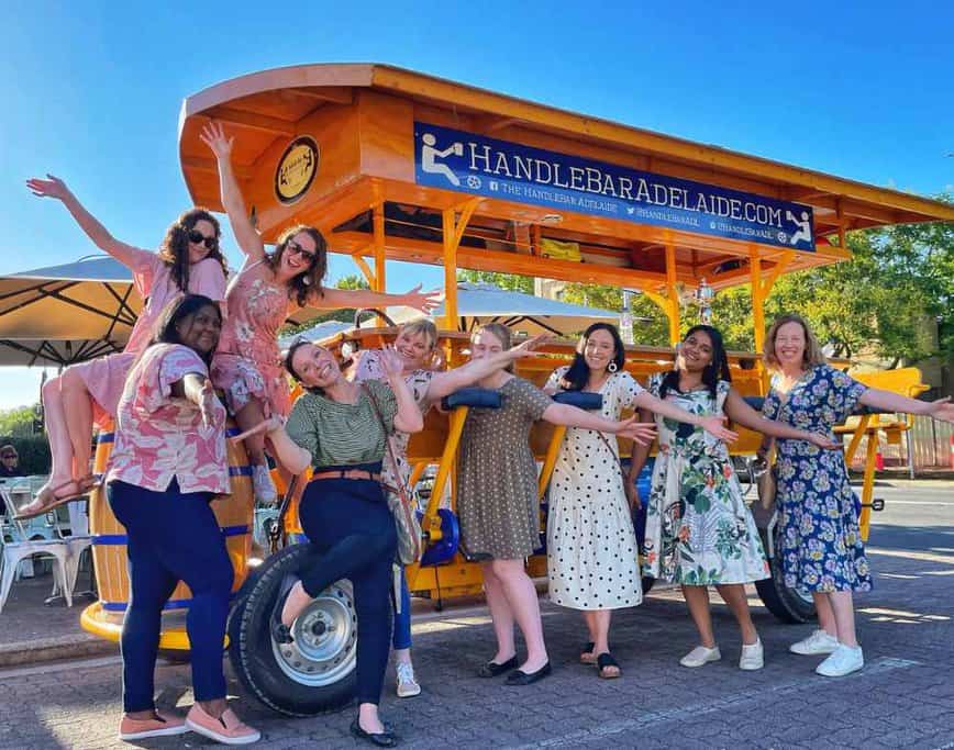 A group of women enjoying a HandleBar Adelaide Progressive Dinner Tour, posing in front of the pedal-powered vehicle. This image highlights the fun and social experience of exploring Adelaide's food scene, with stops at three renowned restaurants for a culinary adventure.