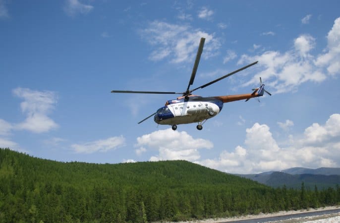Helicopter flying over lush green forests near a river, capturing the breathtaking views of the Grampians on a scenic helicopter tour.