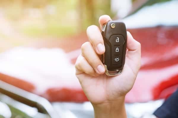A woman holding car keys with a rental car in the background, symbolizing the ease and readiness of renting a car on the Gold Coast.