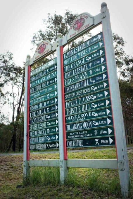 A signpost in Hunter Valley Wine Country pointing to various wineries, restaurants, and accommodations, surrounded by bushland. This image highlights the abundance of local attractions, showcasing one of the lifestyle benefits discussed in the blog post about the pros and cons of living in Hunter Valley.