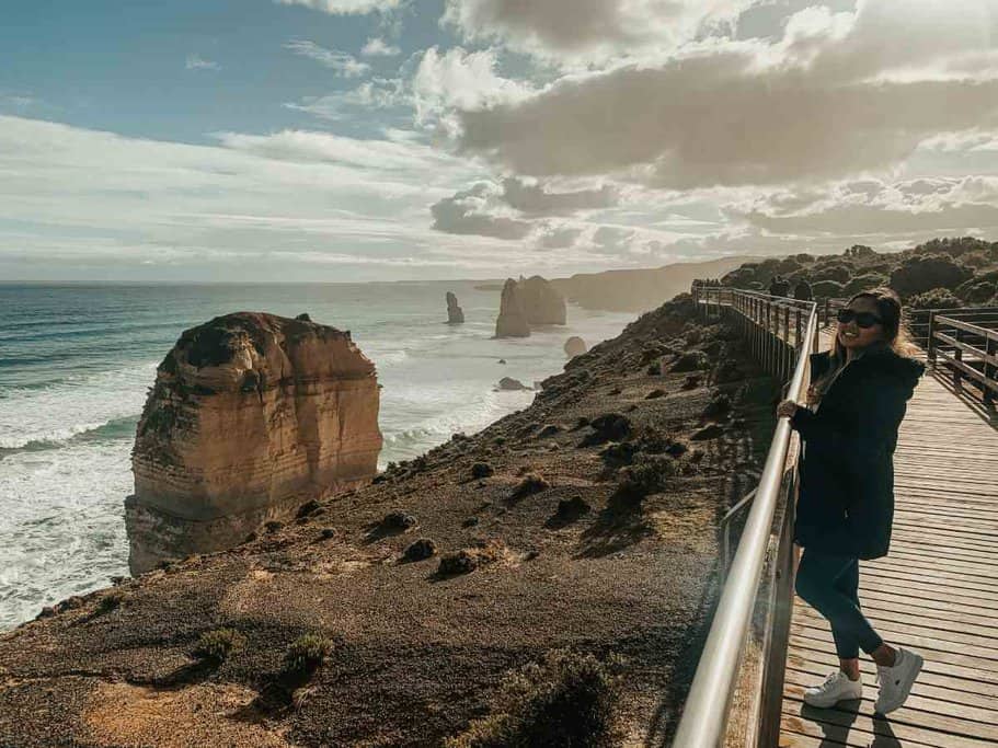 Me leaning on the railing of a wooden boardwalk at the Twelve Apostles on the Great Ocean Road, a breathtaking sight and a popular thing to do near Melbourne in winter.
