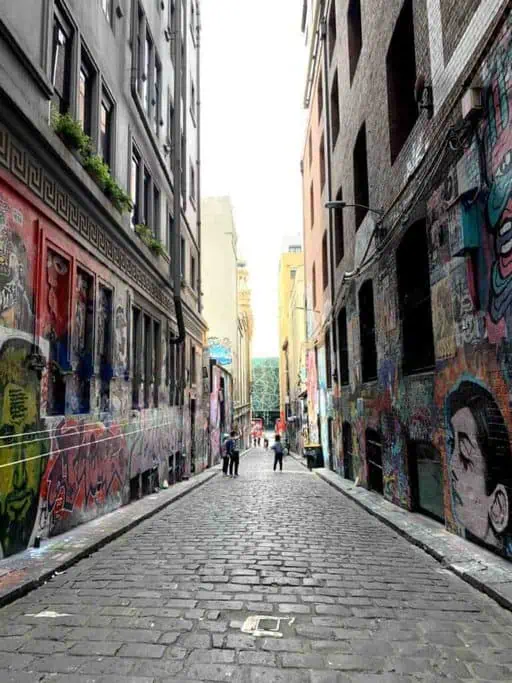A cobblestone street in Melbourne's famous Hosier Lane, adorned with vibrant street art and graffiti on both sides. This laneway is part of Melbourne’s Most Instagrammable Locations, offering a unique and colourful backdrop perfect for capturing artistic photos.