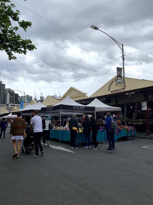 People browsing stalls at Queen Victoria Market in Melbourne, with tents set up and various goods on display. This bustling market is one of the Most Instagram-worthy Places in Melbourne, offering vibrant scenes perfect for capturing the local culture and atmosphere.