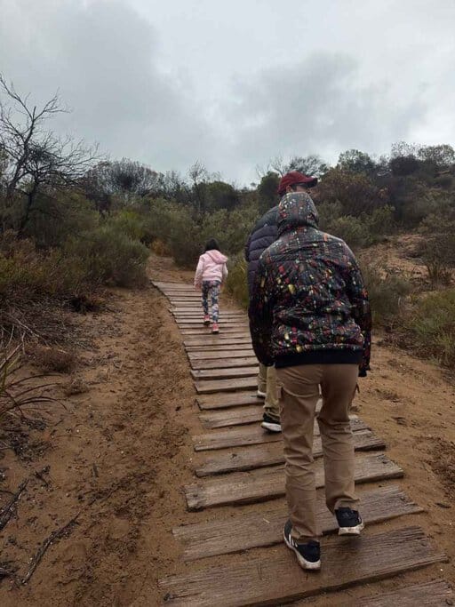 Our family walking along the sandy boardwalk trail through coastal scrub on the way to Waitpinga Beach, just beyond the dunes from Waitpinga beach campground—capturing the natural setting and easy access to the shoreline from the campsites.